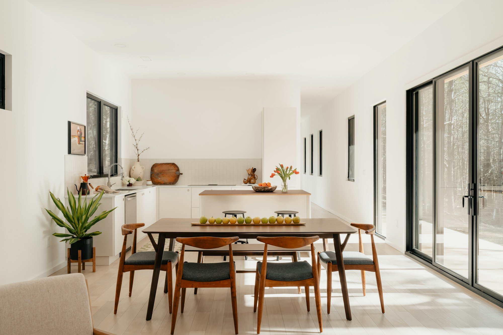 Une salle à manger ouverte sur la cuisine, avec de grandes baies vers le jardin