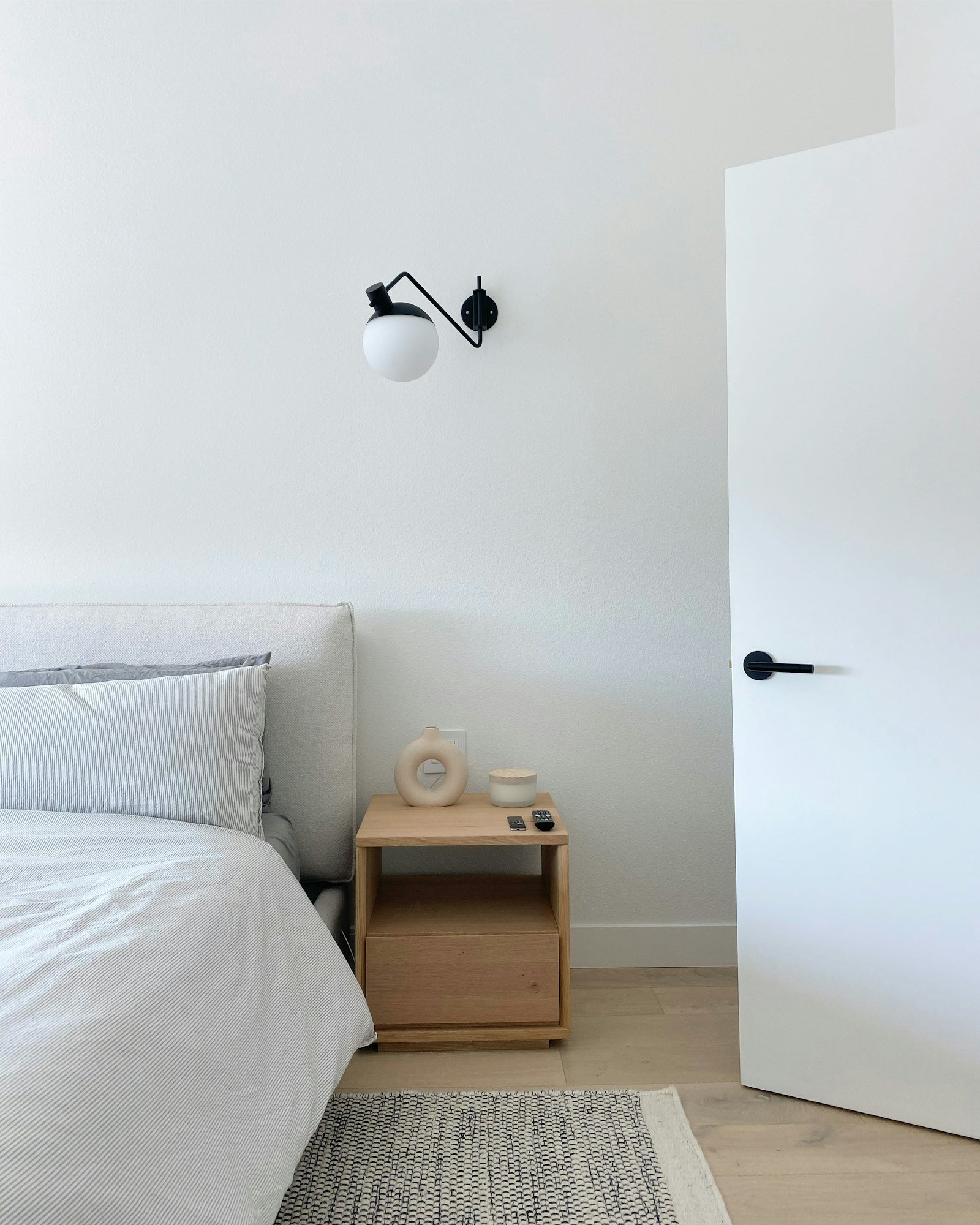 Une chambre blanche et épurée, avec une table de chevet en bois clair