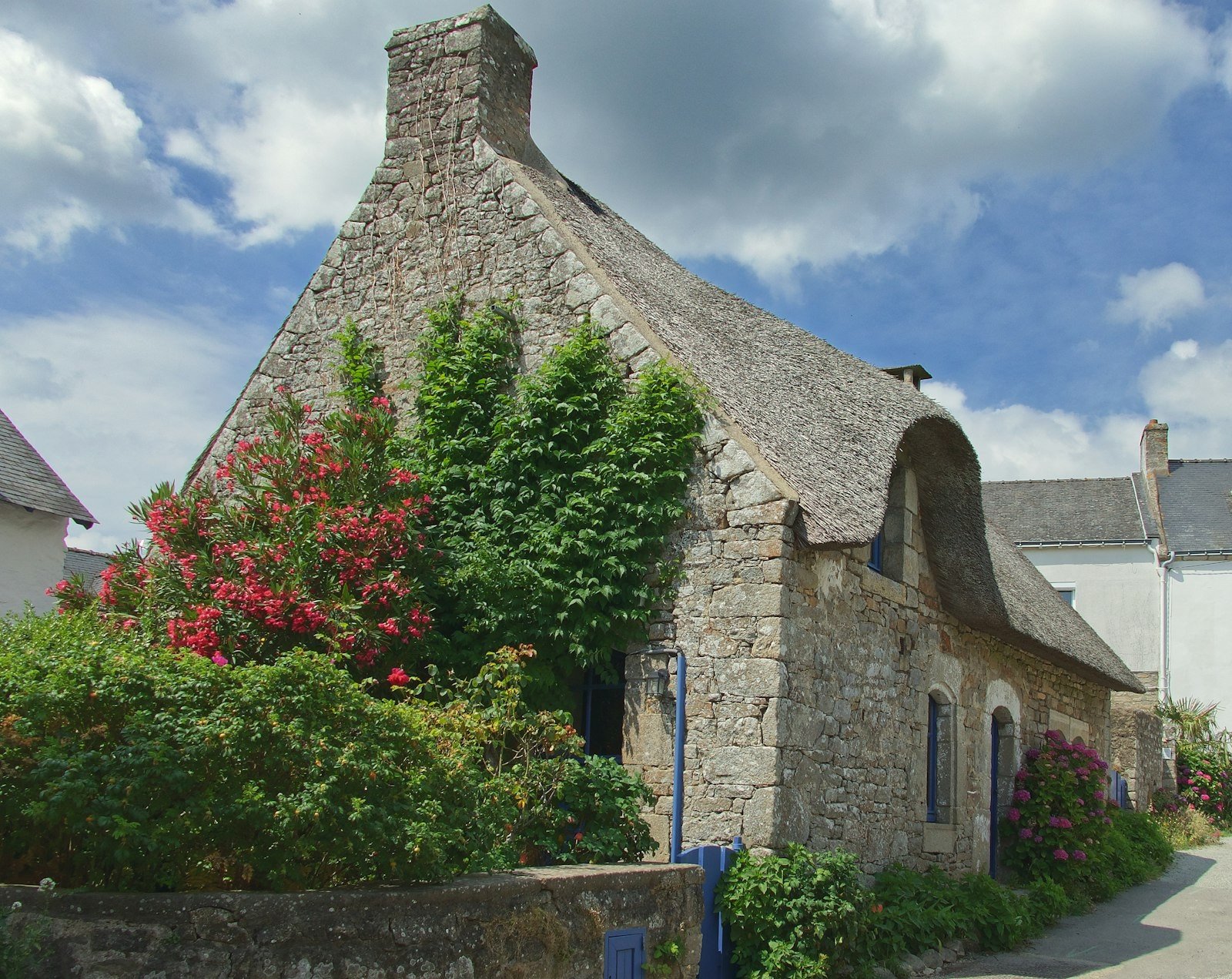 A stone thatched cottage with blue shutters and a flowering garden