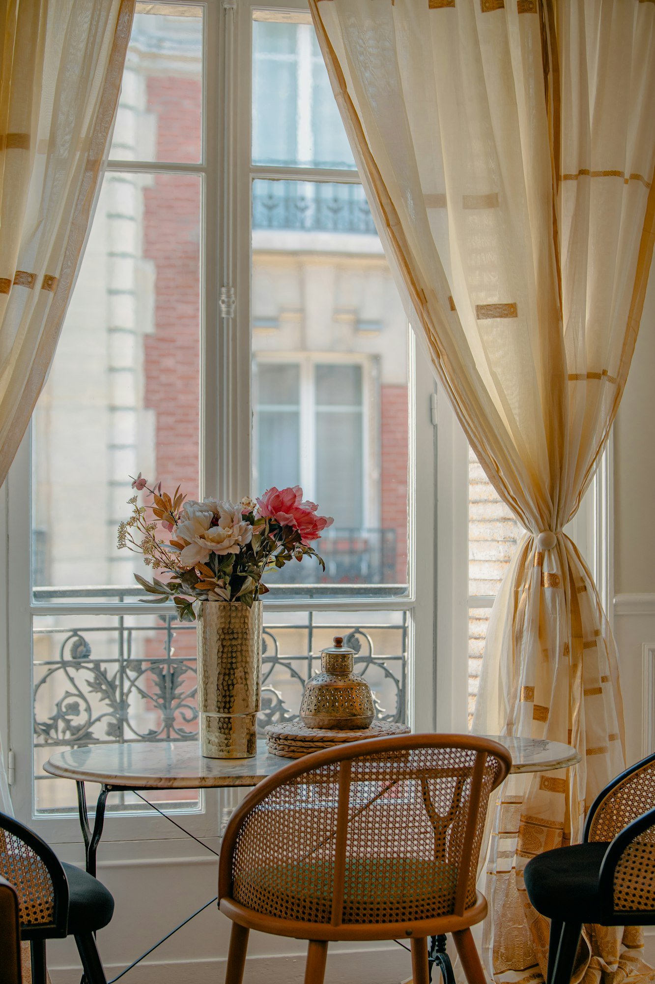 Une table et des chaises cannées devant une porte-fenêtre ouvrant sur un balcon en fer forgé