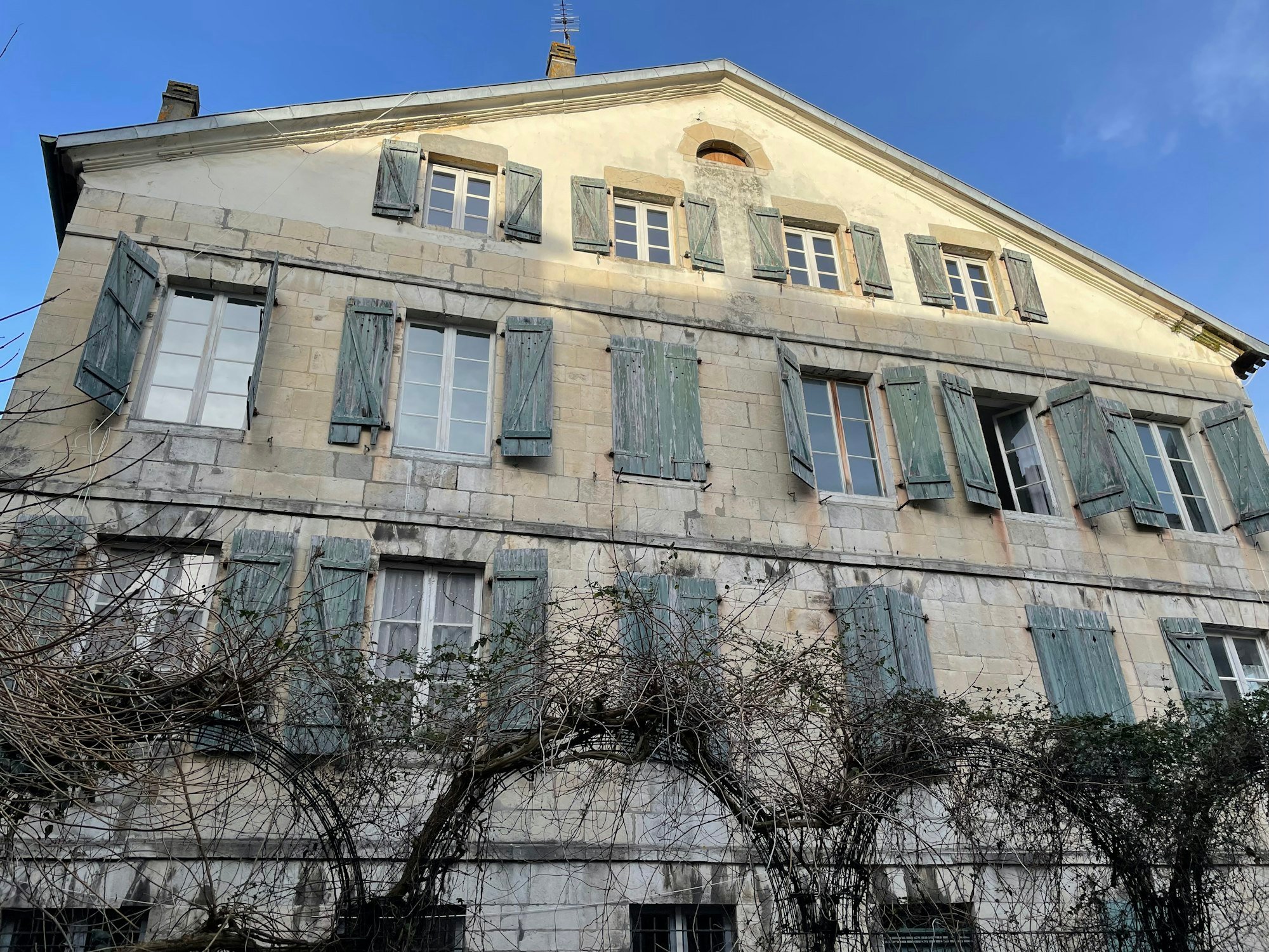 La façade en pierre d’une maison de maître aux volets verts