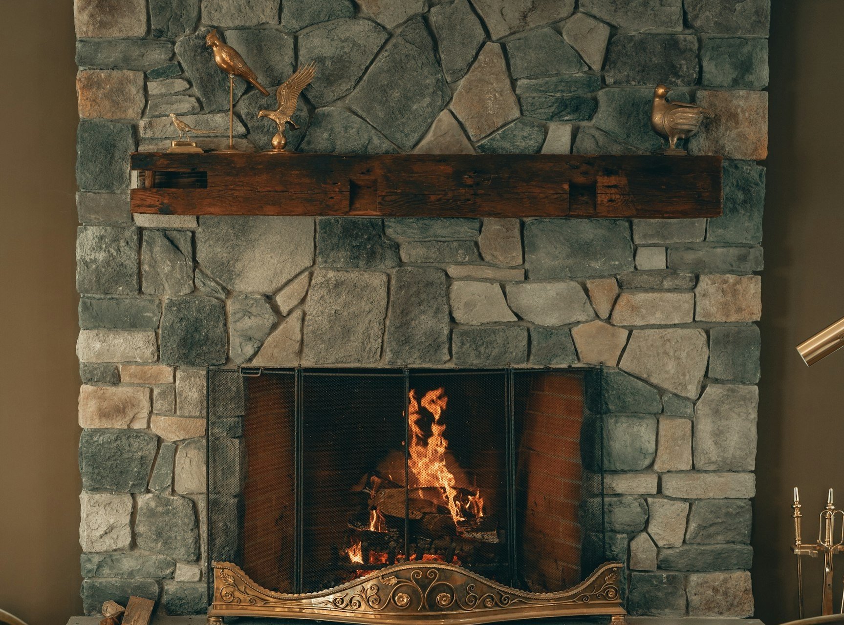 Une cheminée en pierre avec une poutre en bois, entre deux fauteuils