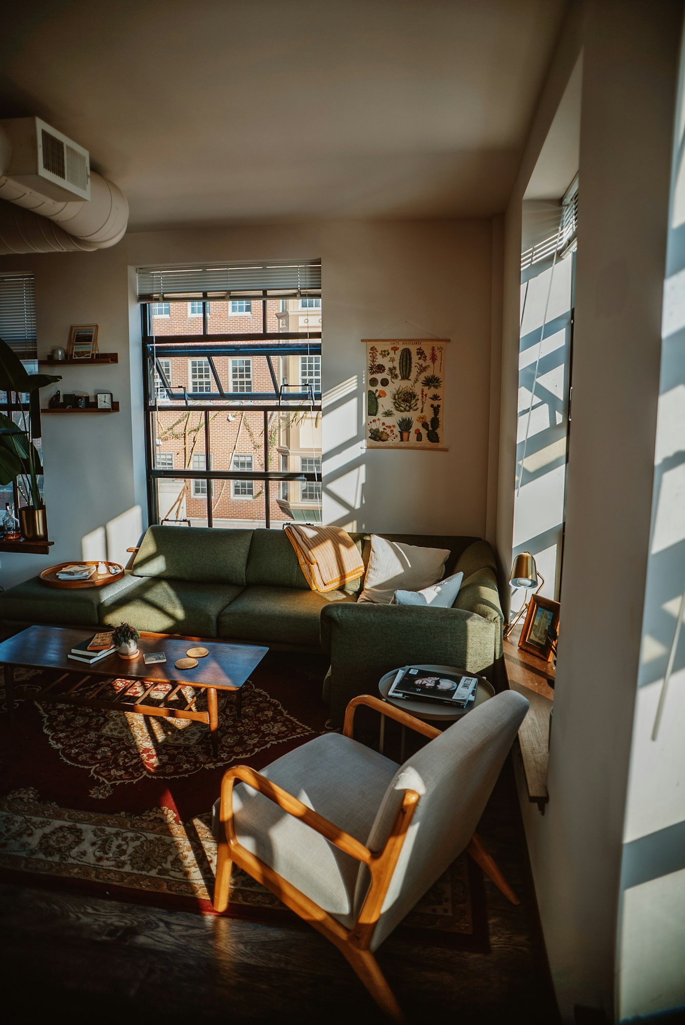 Un loft aux murs blancs et gaines apparentes, avec un canapé vert sous la fenêtre