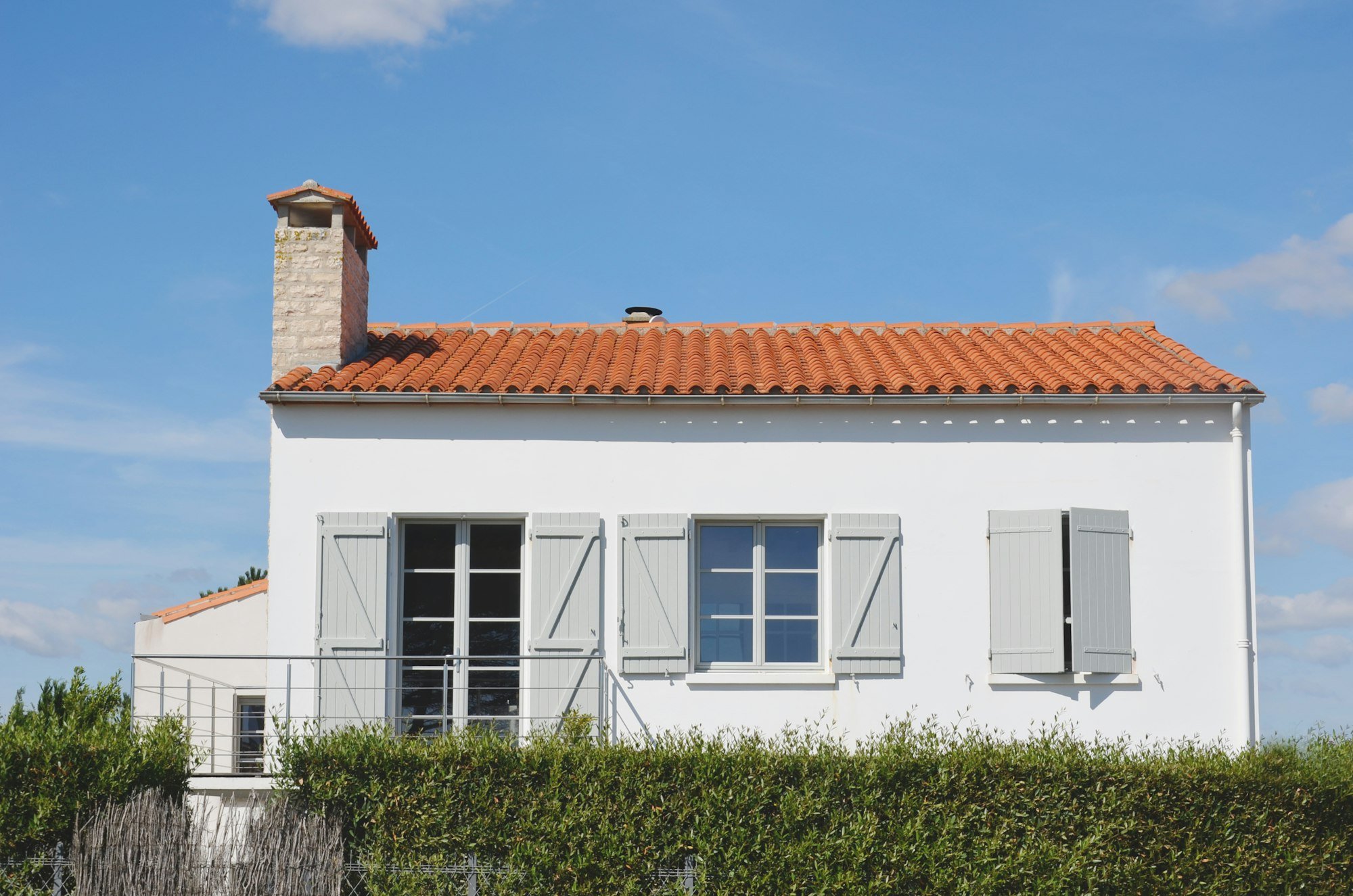 A white house with grey shutters behind a hedge